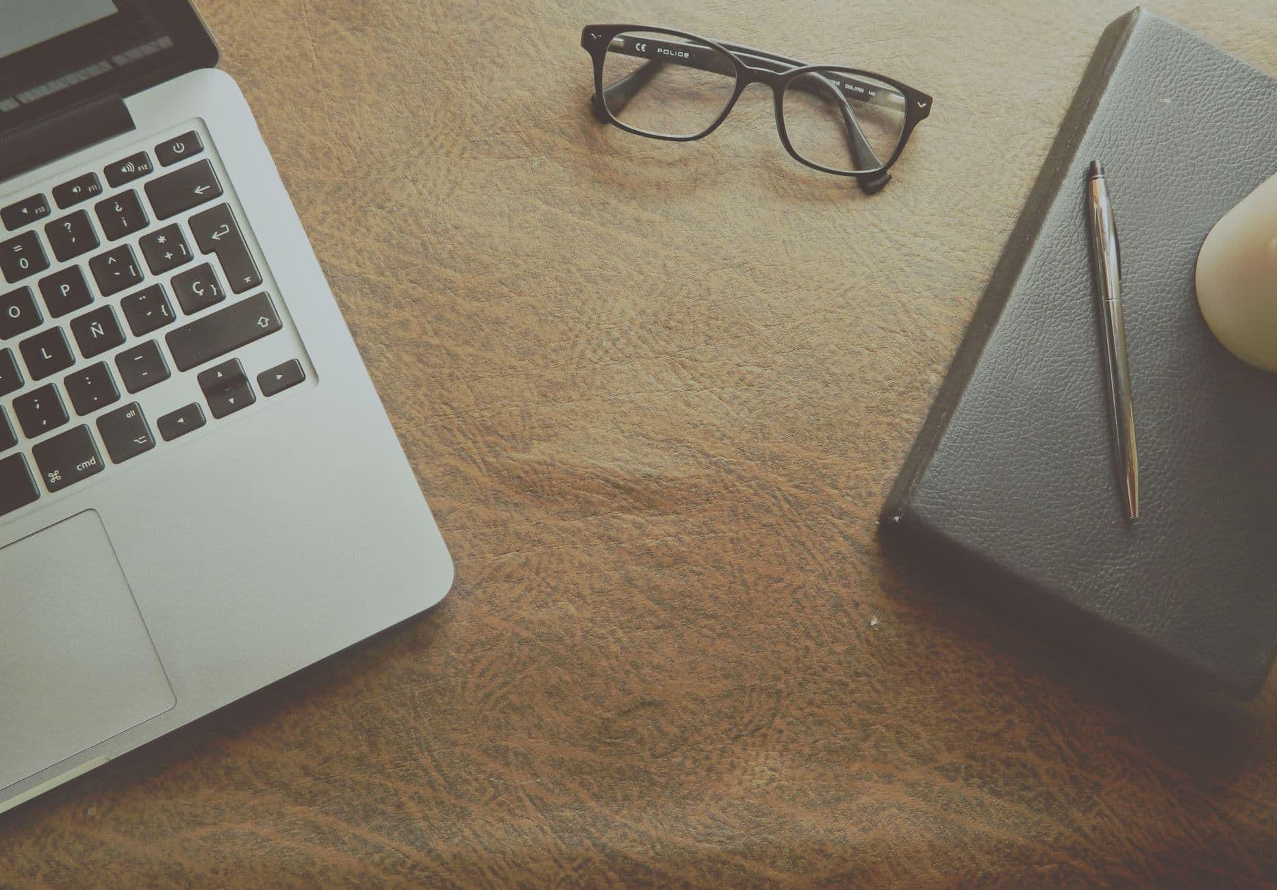 A well-organized workspace featuring a laptop, notebook, and glasses on a leather surface.