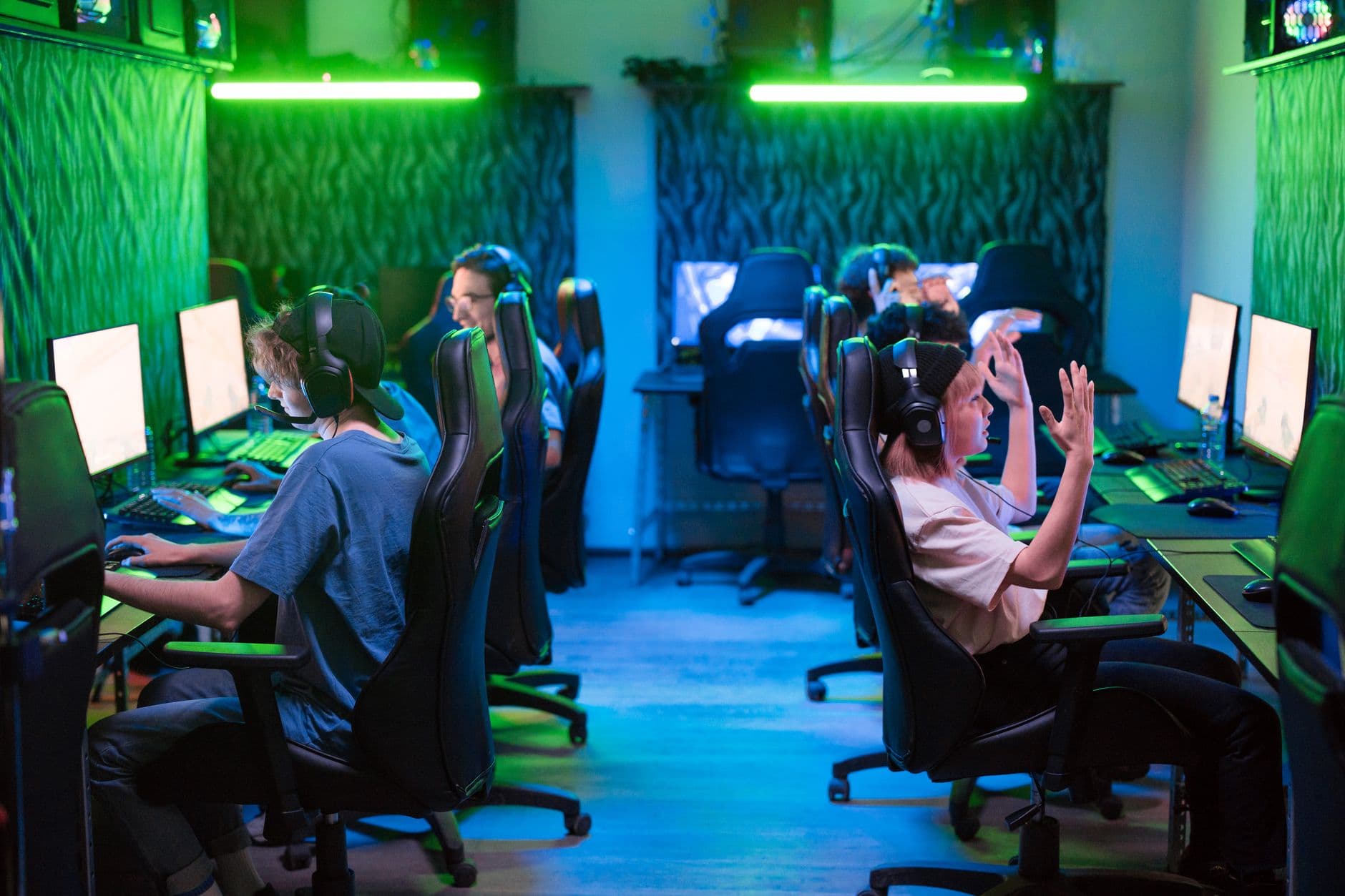Group using computers at a gaming center with green lighting and headphones, teamwork concept.